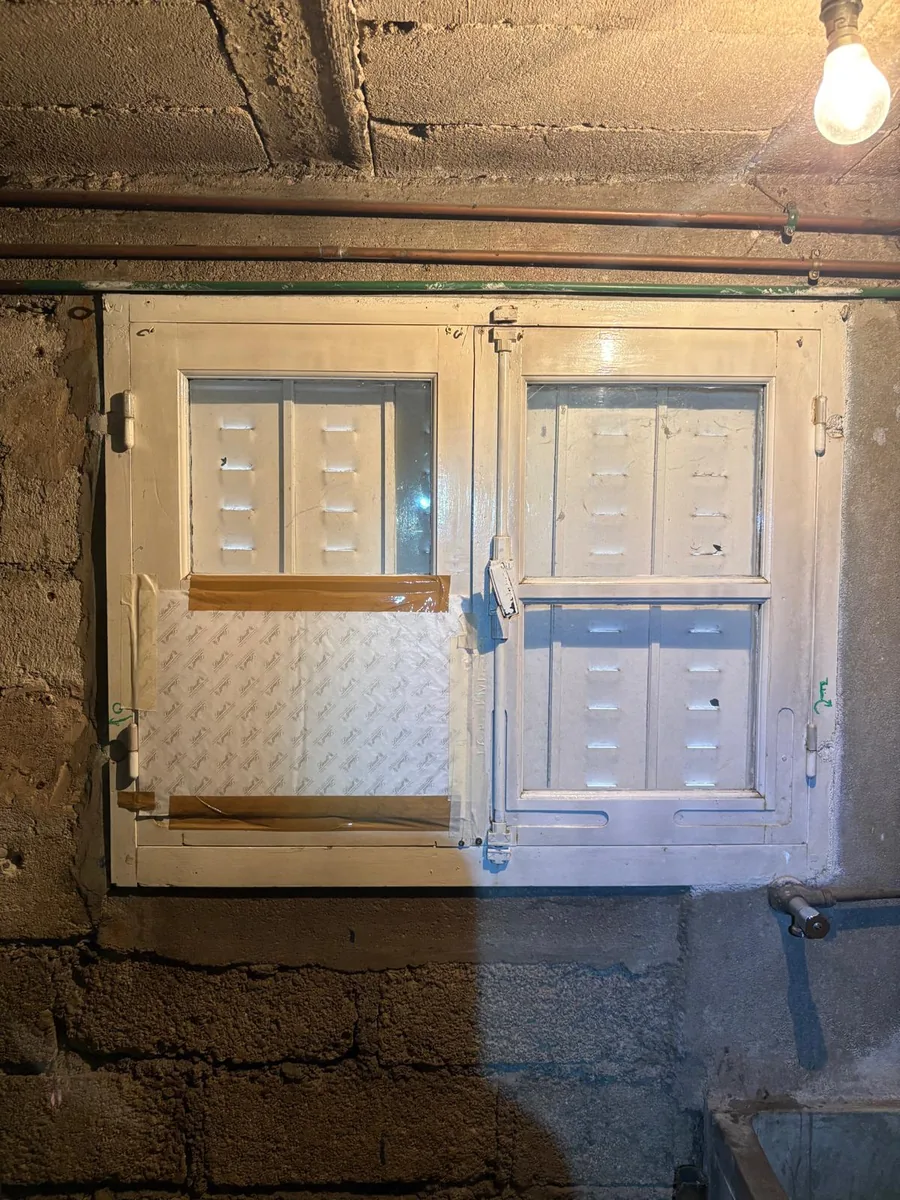 Ancienne fenêtre de cave en bois, vitre cassée et bouchée au carton et à l&rsquo;adhésif